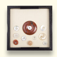 Jasper Mourning Button, in the box surrounded by buttons of loved ones secured with crystal pins. Sizes: L x W = about 125 x 125mm.