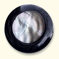 An onyx Mourning Button with a mother of pearl button of a loved one on it. The onyx is always uniformly black.